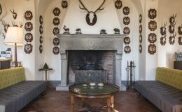 Cozy living room featuring a stone fireplace, two gray sofas, and a round coffee table, adorned with mounted deer antlers and decorative plaques on the walls.