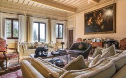 Elegant living room featuring plush sofas, a wooden coffee table, and large windows with natural light. The space is adorned with classic decor, including a large painting and decorative accents, creating a warm and inviting atmosphere.