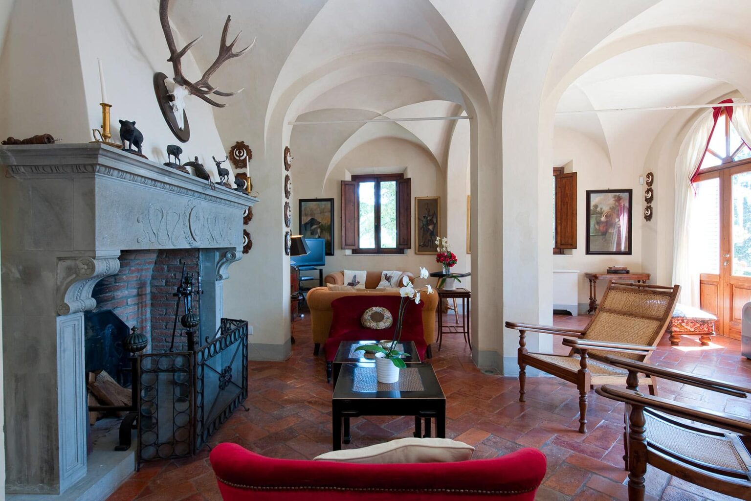 Spacious living room with arched ceilings, a stone fireplace, and rustic decor, featuring comfortable seating and natural light from large windows. | Only on SopranoVillas