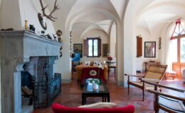 Spacious living room with arched ceilings, a stone fireplace, and rustic decor, featuring comfortable seating and natural light from large windows.