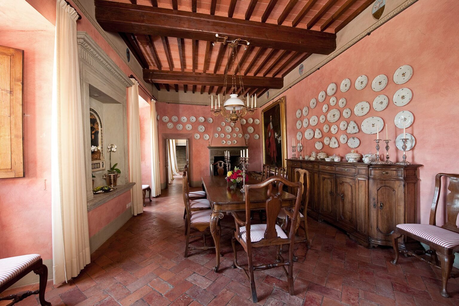 Dining room with rustic wooden furniture, pink walls adorned with decorative plates, and exposed wooden beams, creating a warm and inviting atmosphere. | Only on SopranoVillas