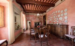 Dining room with rustic wooden furniture, pink walls adorned with decorative plates, and exposed wooden beams, creating a warm and inviting atmosphere.