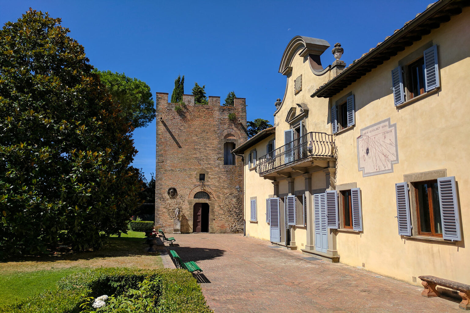 Historic villa and tower in a scenic garden under a clear blue sky, showcasing traditional architecture with stone walls and wooden shutters. | Only on SopranoVillas