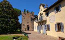 Historic villa and tower in a scenic garden under a clear blue sky, showcasing traditional architecture with stone walls and wooden shutters.