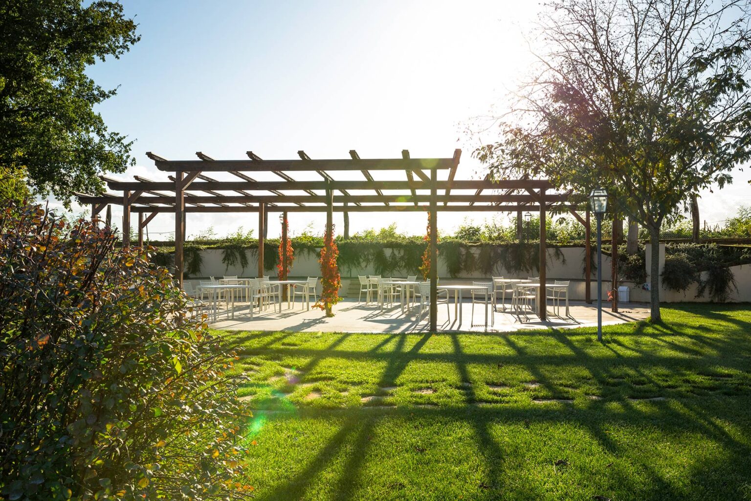 Outdoor event space featuring a wooden pergola surrounded by lush greenery and sunlight, ideal for weddings and gatherings. | Only on SopranoVillas