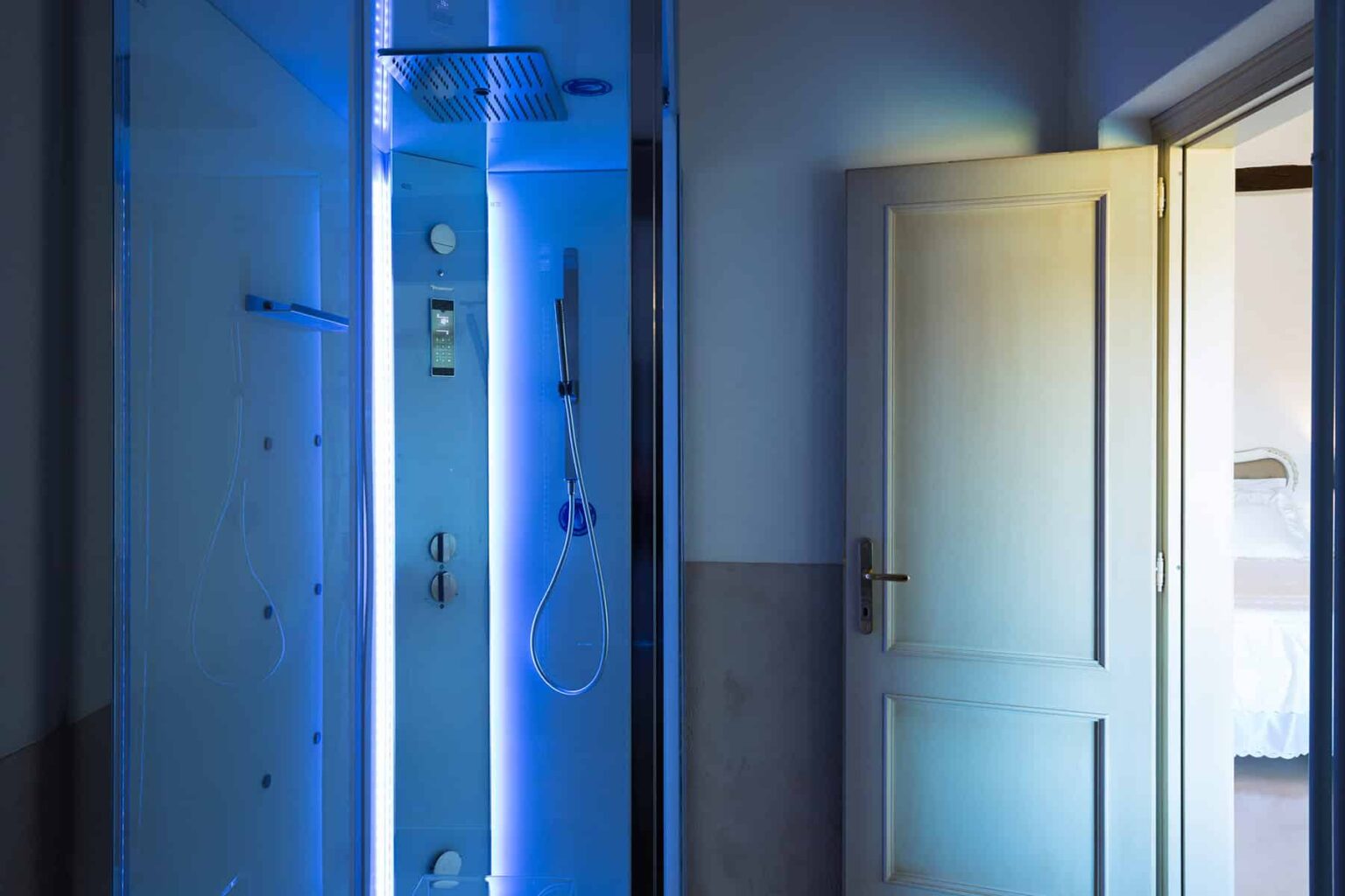 Modern bathroom featuring a sleek shower with blue LED lighting and an open door leading to another room, showcasing contemporary design elements. | Only on SopranoVillas