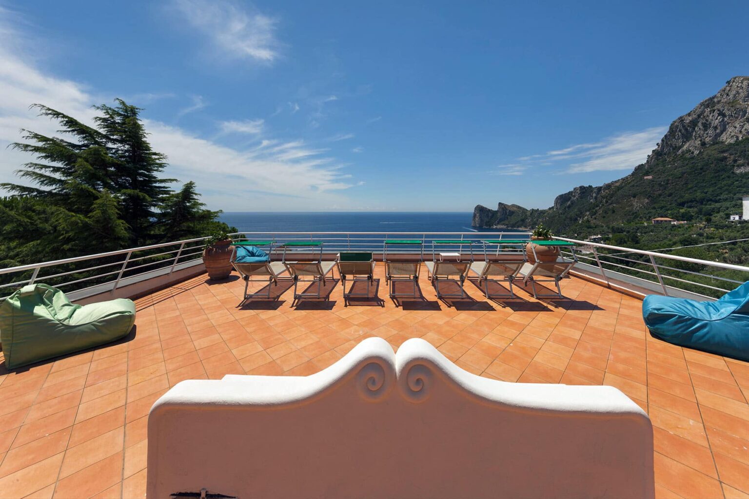 Spacious outdoor terrace with sun loungers and bean bags overlooking the ocean and mountains, ideal for relaxation and enjoying scenic views. | Only on SopranoVillas