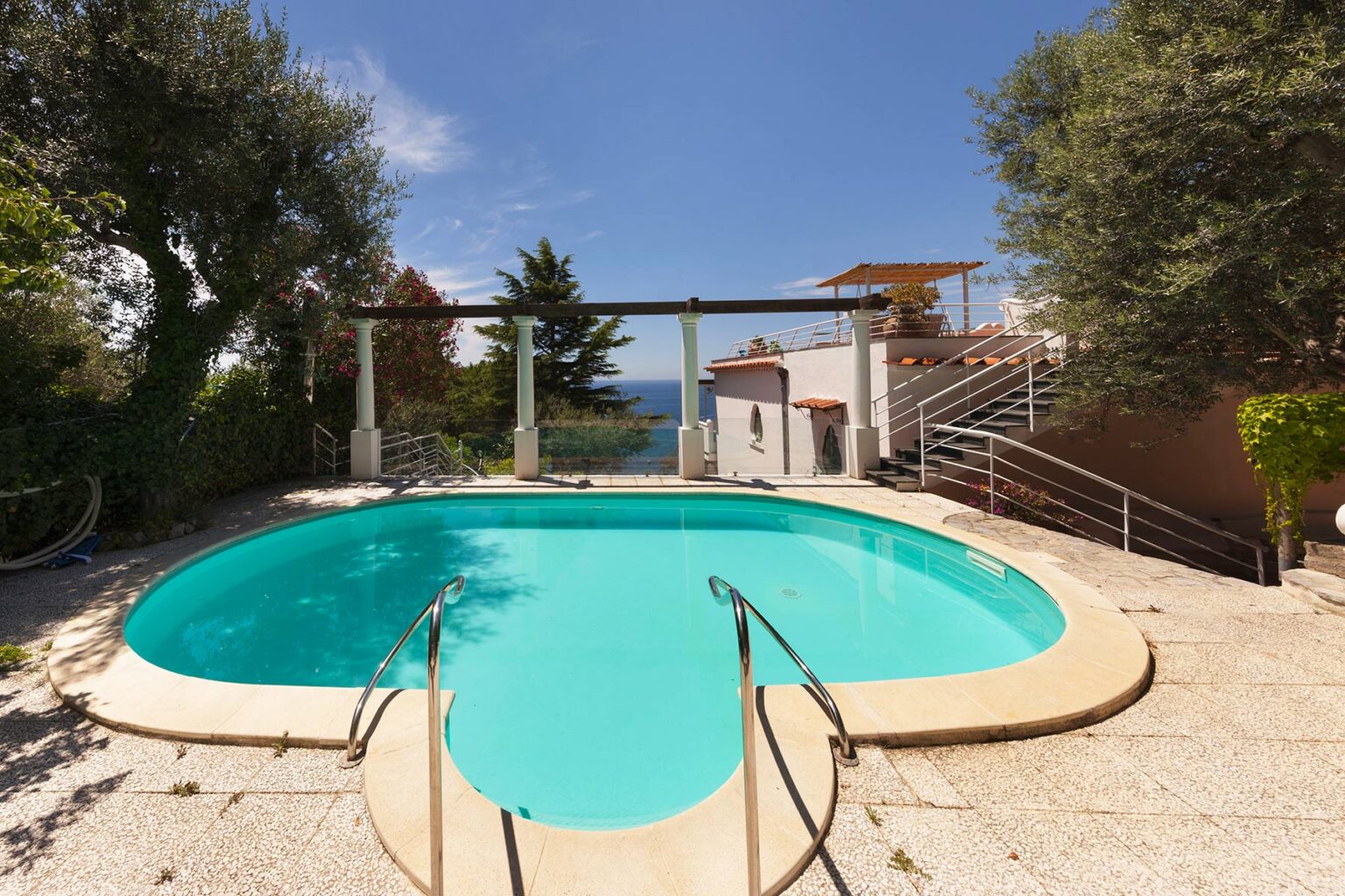 Luxury outdoor swimming pool surrounded by lush greenery and scenic views, featuring a unique heart-shaped design and steps leading into the water. Ideal for relaxation and leisure in a tranquil setting. | Only on SopranoVillas