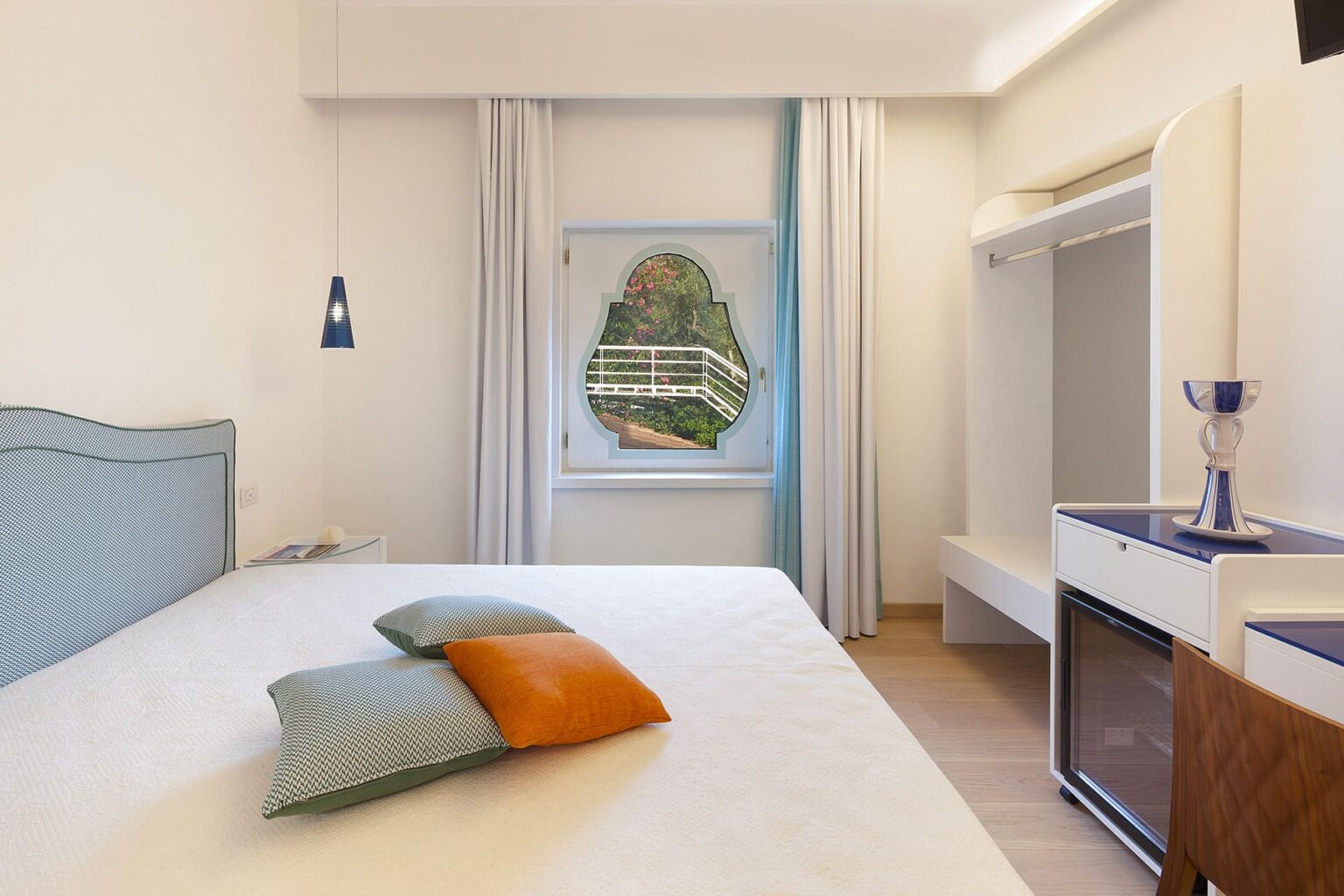 Modern bedroom interior featuring a large bed with decorative cushions, a stylish window with scenic views, and minimalist furniture. The room is bright and inviting, highlighting a relaxed atmosphere ideal for comfort and rest. | Only on SopranoVillas