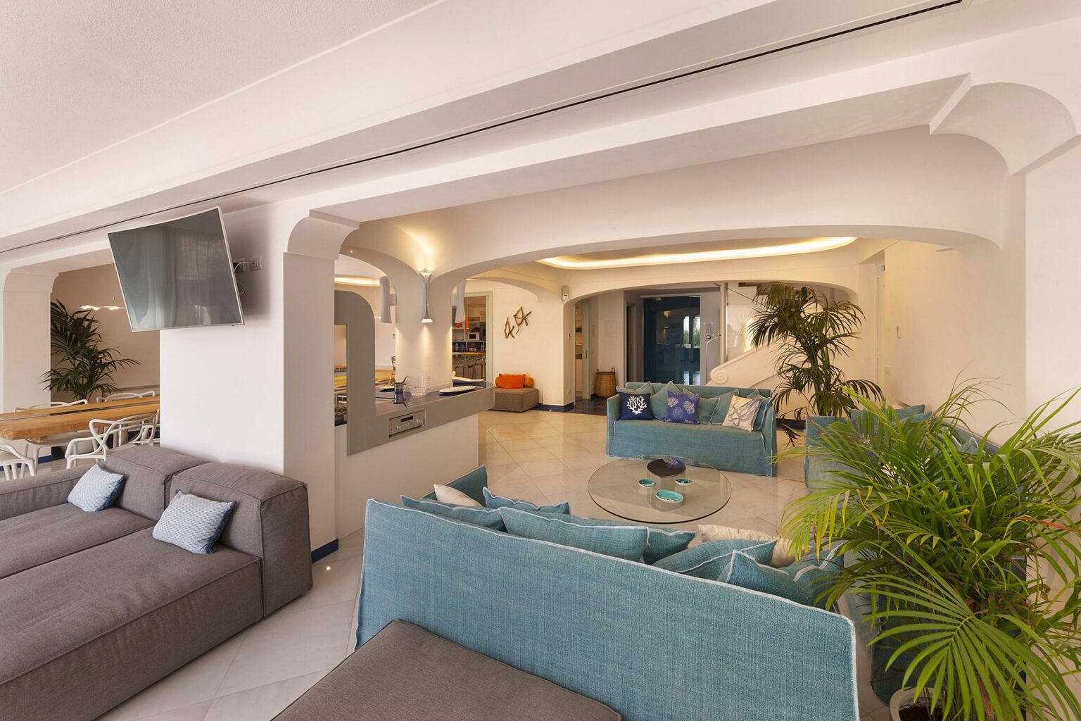 Modern living room interior featuring comfortable seating, a glass coffee table, and decorative plants, with an open layout and natural light. Ideal for relaxation and social gatherings. | Only on SopranoVillas