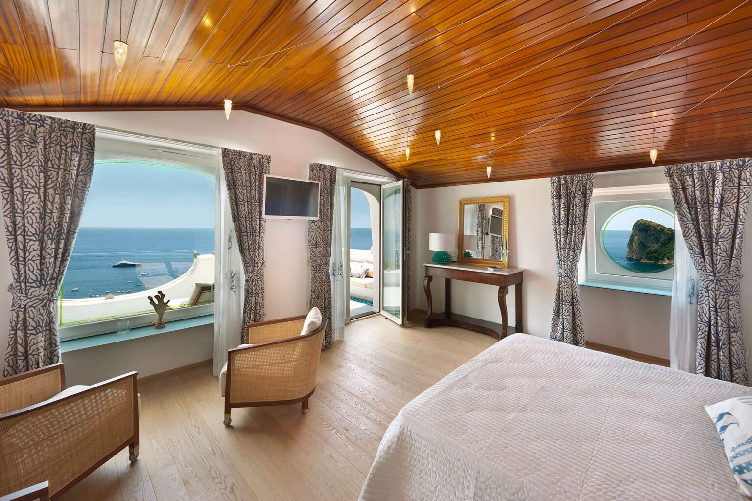 Cozy seaside bedroom with wooden ceiling, large windows offering ocean views, stylish furniture, and natural light. Perfect for a relaxing getaway. | Only on SopranoVillas