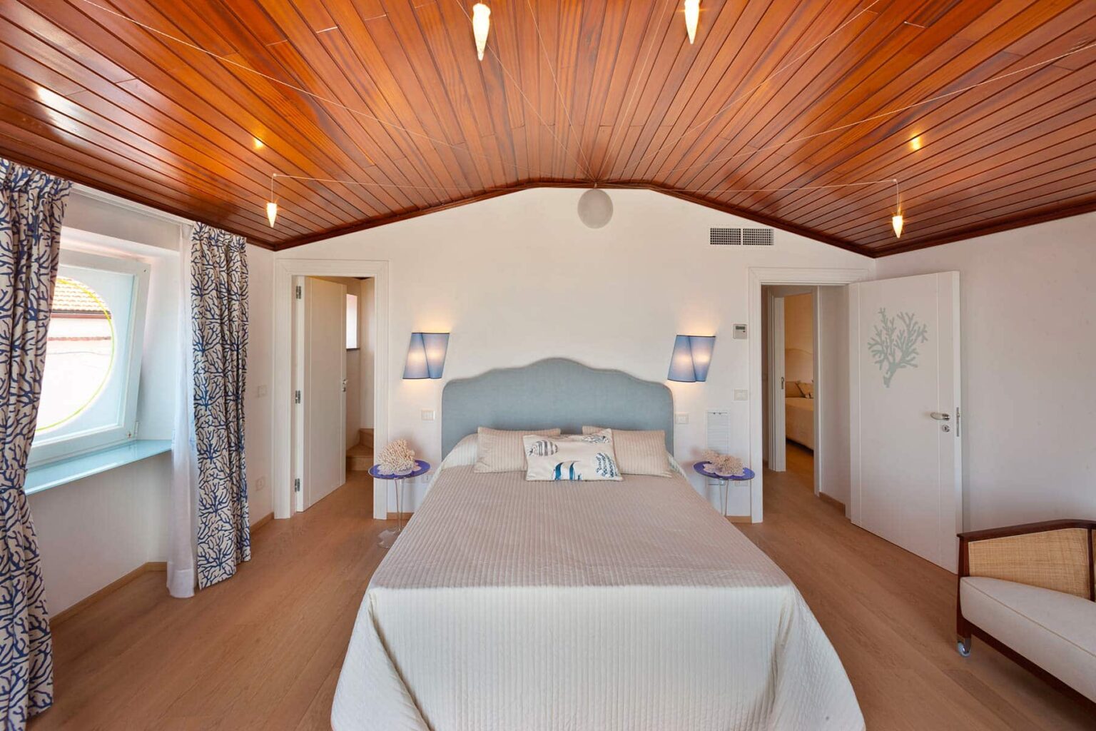 Cozy bedroom interior featuring a light blue headboard, wooden ceiling, and natural light from windows, designed for a relaxing atmosphere. | Only on SopranoVillas