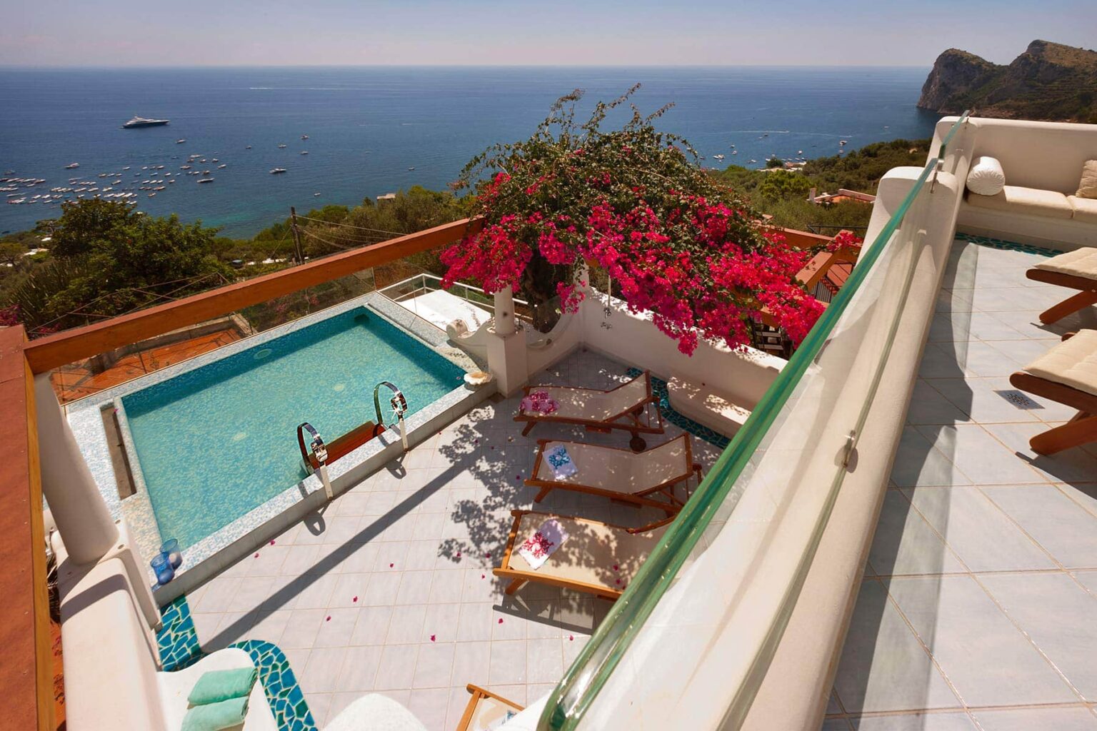 Luxurious villa terrace overlooking the ocean, featuring a private plunge pool, vibrant bougainvillea, and sun loungers, perfect for relaxation and enjoying scenic views. | Only on SopranoVillas