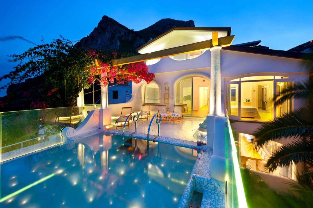 Luxurious villa with a sparkling pool and vibrant landscaping, illuminated at dusk, showcasing modern architecture and stunning mountain views. Ideal for relaxation and upscale getaways. | Only on SopranoVillas