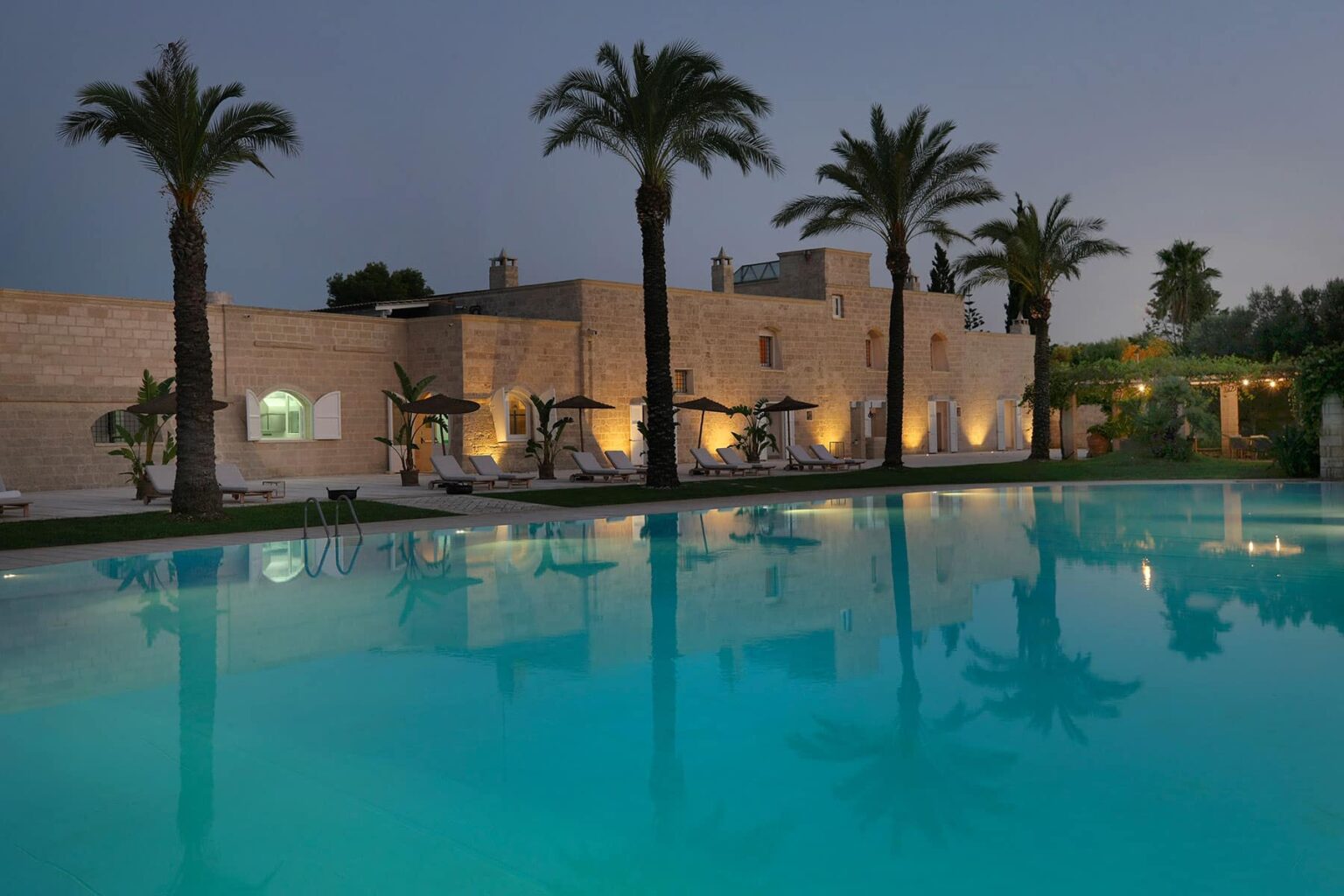 Luxurious villa with palm trees and a serene swimming pool at dusk, showcasing tranquil outdoor living and elegant architecture. | Only on SopranoVillas