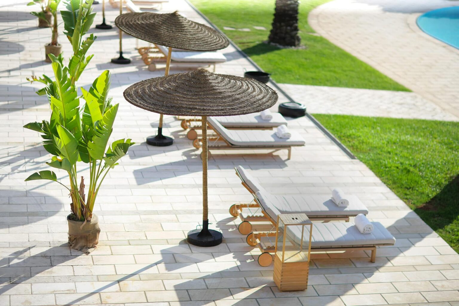 Lounge chairs with umbrellas beside a pool, surrounded by green grass and tropical plants, creating a relaxing outdoor atmosphere. | Only on SopranoVillas