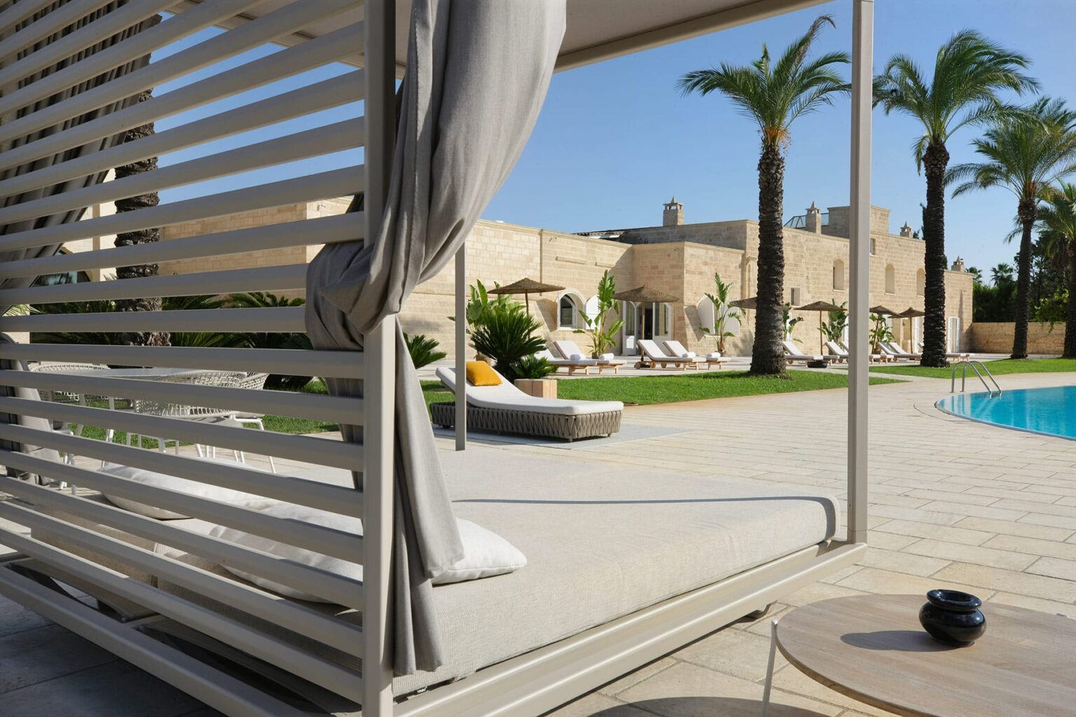 Modern outdoor lounge area with a sleek cabana, palm trees, and a swimming pool, perfect for relaxation and leisure. | Only on SopranoVillas