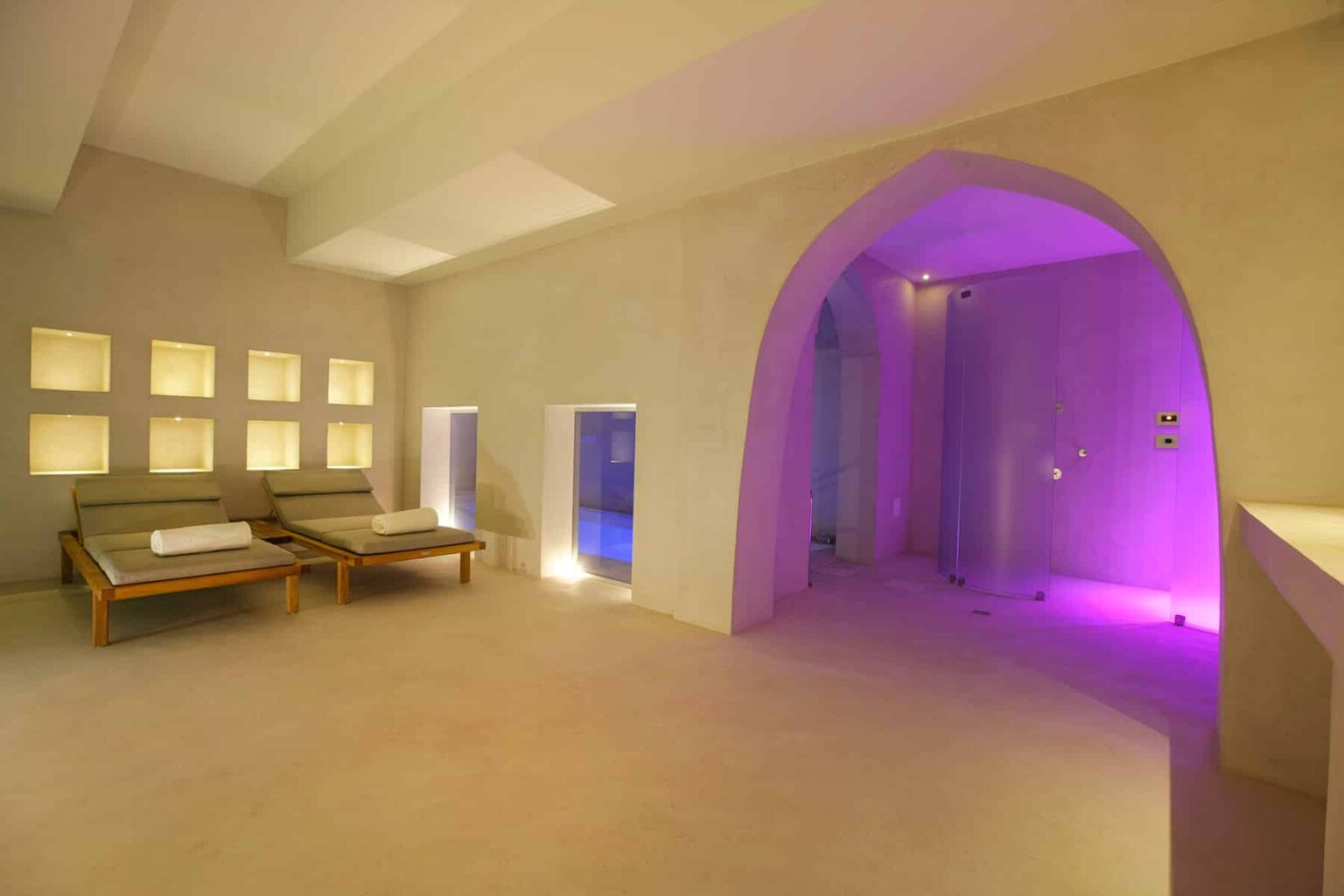 Relaxing wellness spa interior featuring comfortable lounge chairs, soft lighting, and a calming atmosphere. The design includes an arched entryway and colorful ambient lighting, perfect for rejuvenation and tranquility. | Only on SopranoVillas