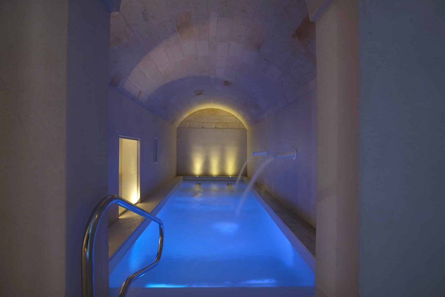 Serene indoor swimming pool with soft blue lighting and elegant arching architecture, creating a tranquil spa atmosphere. | Only on SopranoVillas