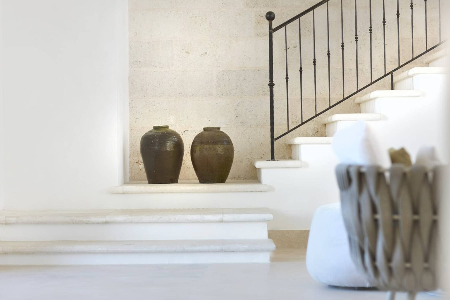 Two decorative dark vases positioned at the base of a staircase in a bright, modern interior, with a stylish woven basket nearby, showcasing a blend of elegance and minimalism. | Only on SopranoVillas