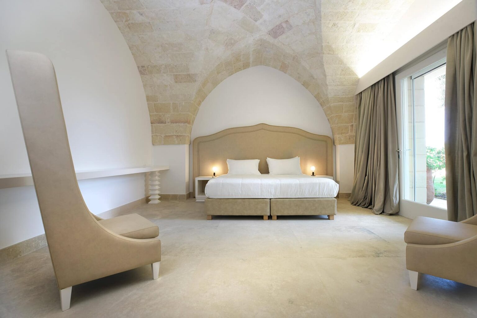 Modern hotel room featuring a king-size bed, elegant beige decor, high arched ceiling, large windows with curtains, and stylish seating. Ideal for a relaxing getaway. | Only on SopranoVillas