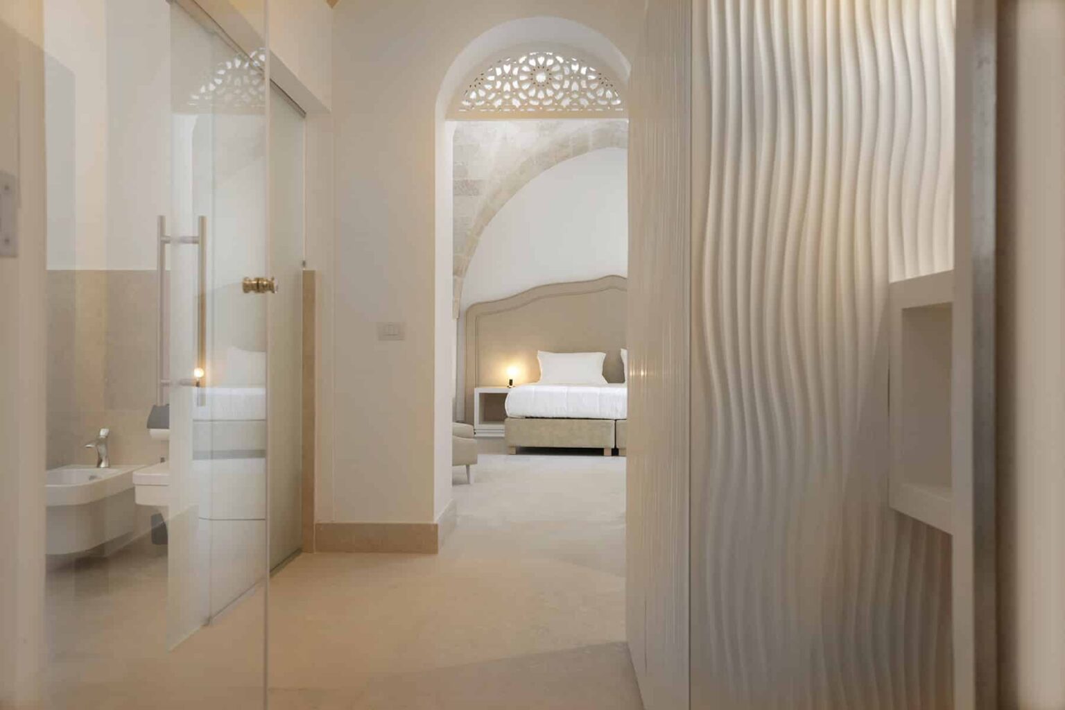 Modern hotel interior showcasing a stylish entrance with a curved glass door leading to a spacious bedroom featuring elegant decor and soft lighting. The design highlights a blend of contemporary and traditional elements. | Only on SopranoVillas