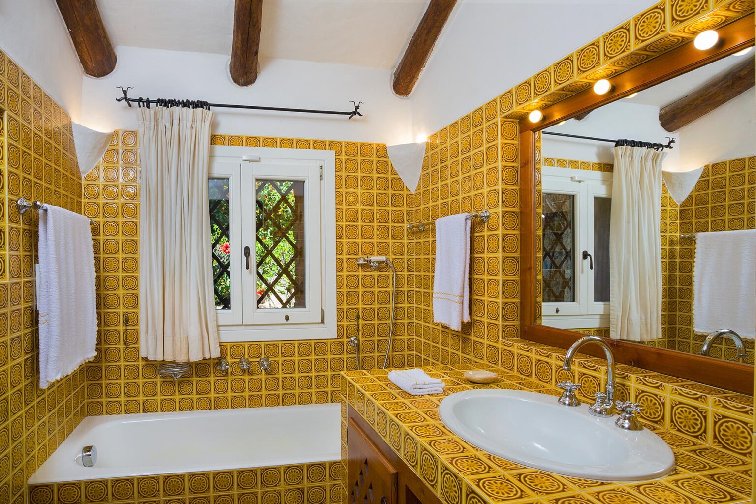 Bright and stylish bathroom featuring yellow tiled walls, a white bathtub, and a modern sink with a wooden mirror. Natural light streams in through a window adorned with cream curtains, enhancing the warm ambiance. | Only on SopranoVillas