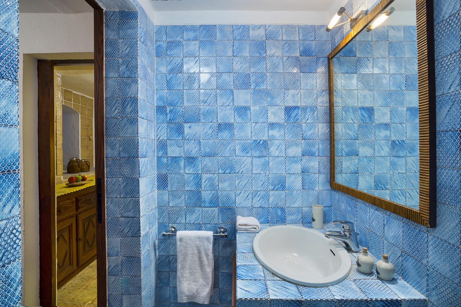 Bright blue tiled bathroom featuring a modern sink, large mirror, and elegant fixtures. The design creates a refreshing and spacious atmosphere, perfect for relaxation. | Only on SopranoVillas