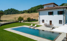 Aerial view of a modern villa with a swimming pool, surrounded by lush green lawns and gentle rolling hills in the background, ideal for vacation rentals or luxury retreats.