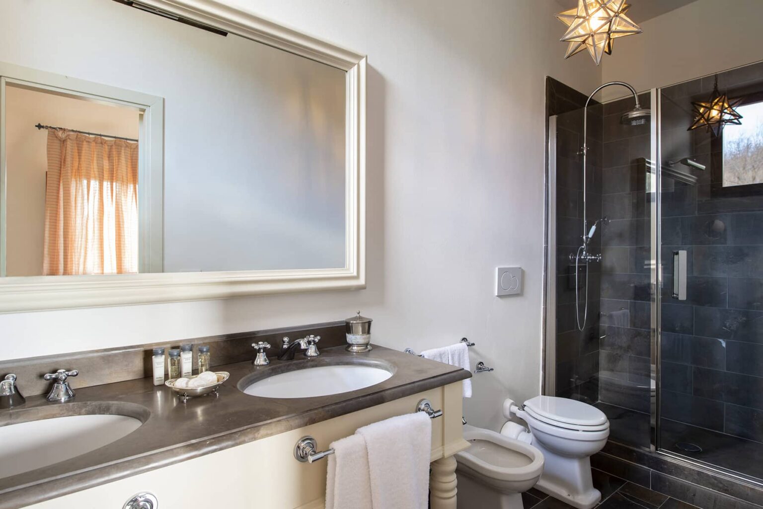 Modern bathroom featuring dual sinks, a large mirror, and a glass shower enclosure with contemporary fixtures, complemented by warm lighting and neutral tones. | Only on SopranoVillas