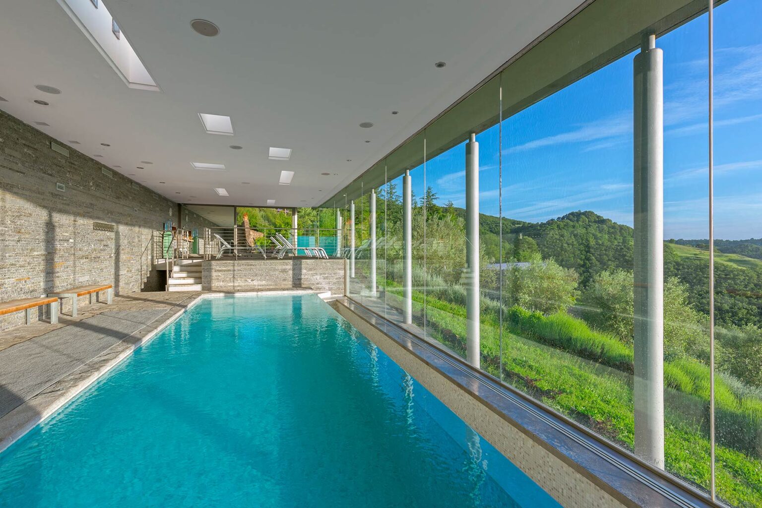 Indoor swimming pool with large glass windows overlooking a lush green landscape, featuring modern design elements and natural light. | Only on SopranoVillas