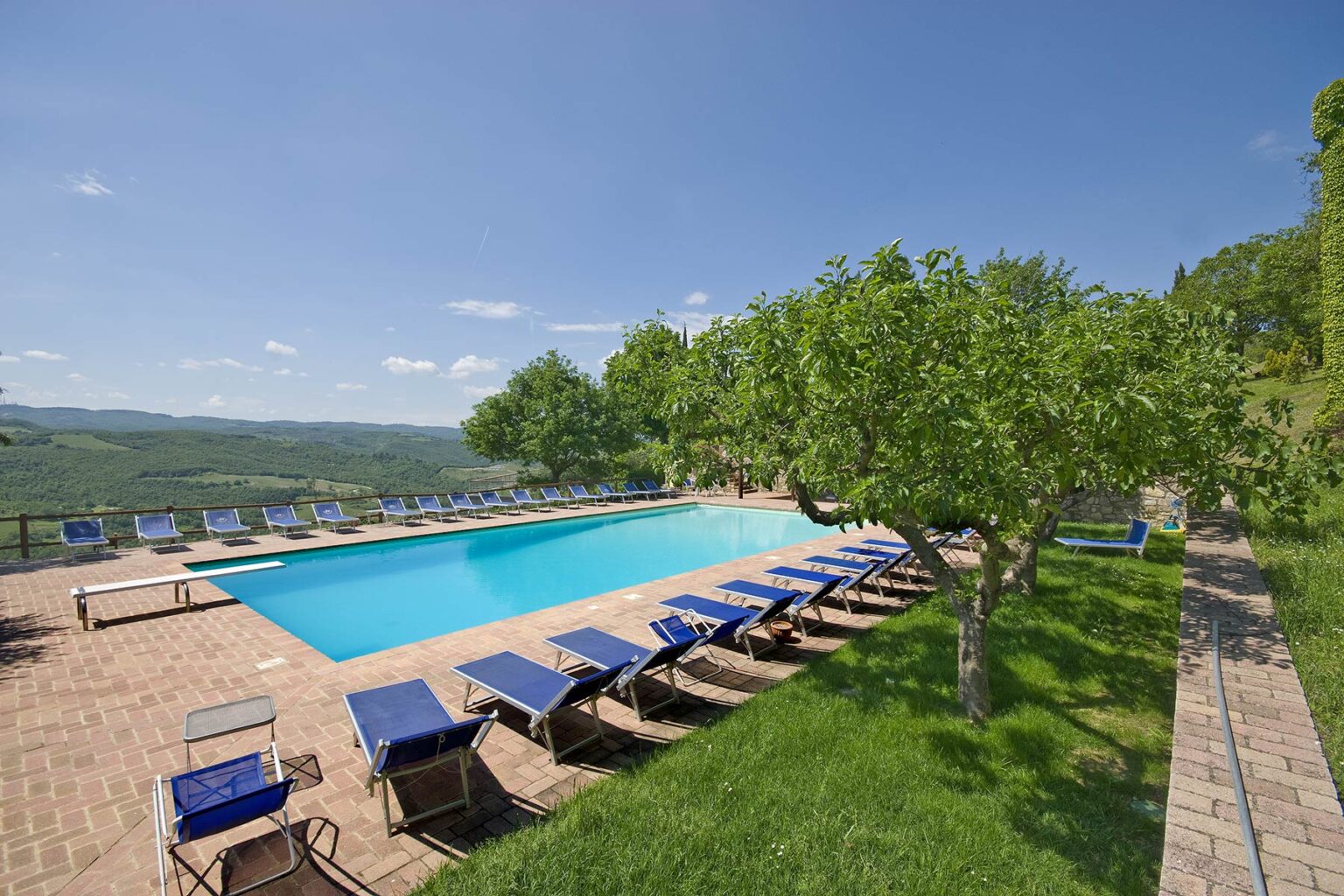 Scenic outdoor swimming pool surrounded by lounge chairs and lush greenery, offering a relaxing atmosphere with beautiful views of the landscape under a clear blue sky. | Only on SopranoVillas