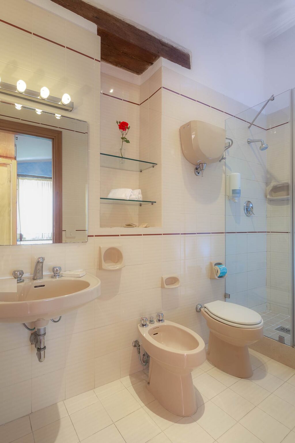 Modern bathroom featuring a glass shower, sink with faucet, and minimalistic shelving. Soft natural light illuminates the space, highlighting the clean design and neutral color palette. | Only on SopranoVillas