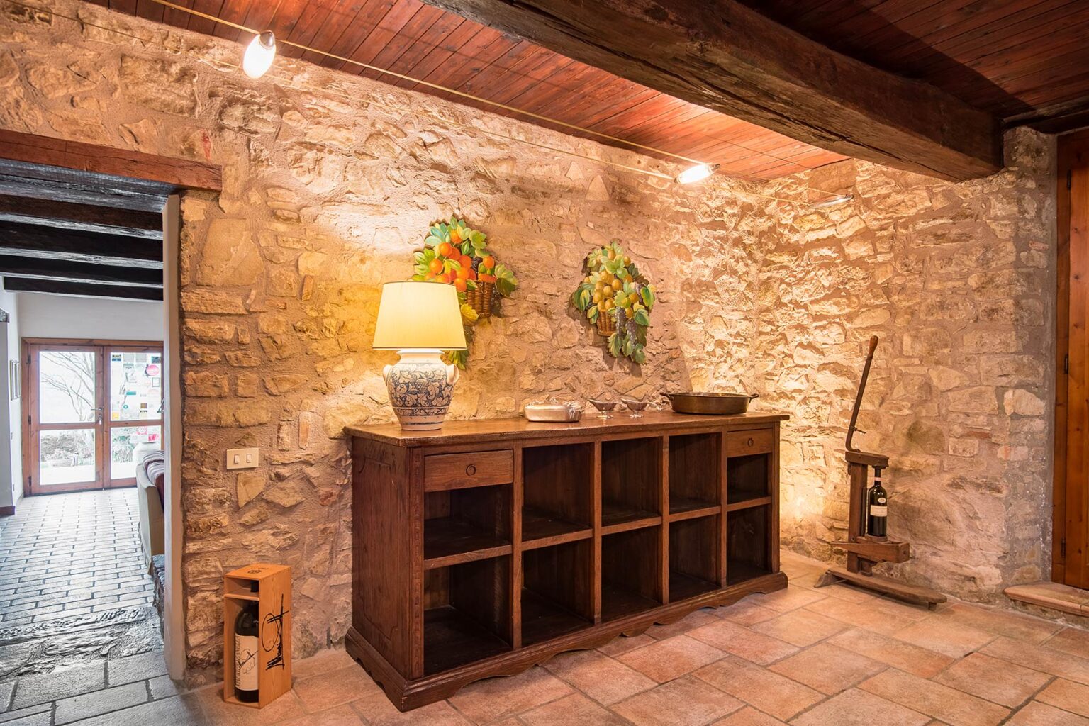 Rustic interior design featuring a stone wall and wooden furniture, including a console table with a lamp and decorative plants, creating a cozy atmosphere in a home setting. | Only on SopranoVillas