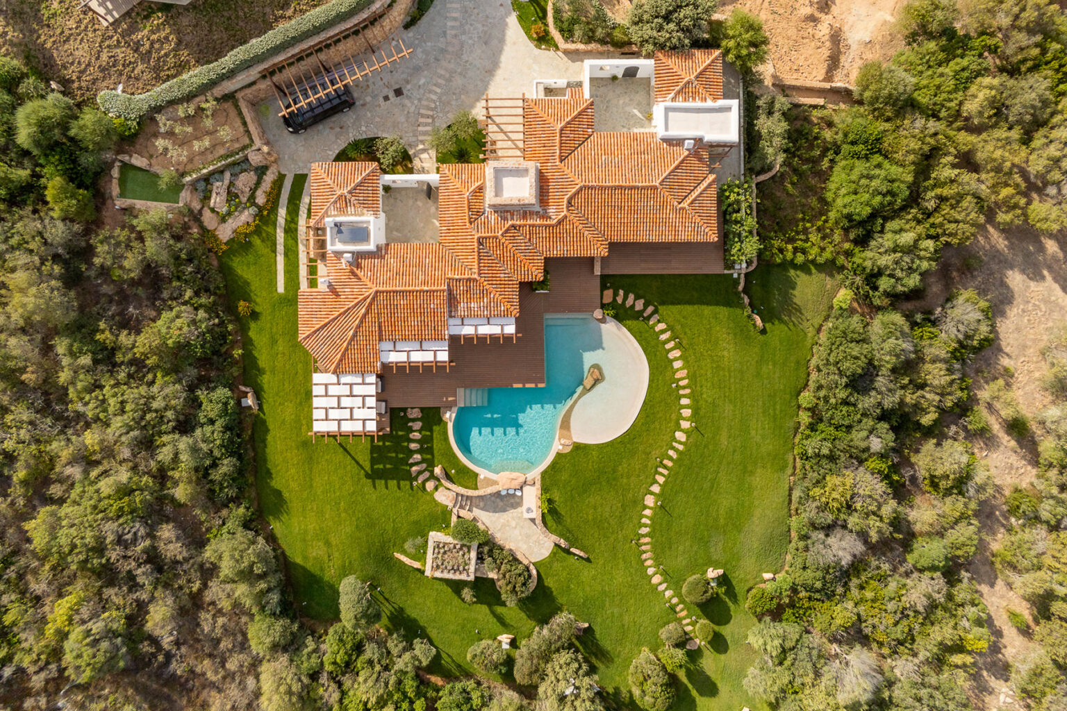 Aerial view of a luxurious villa featuring a spacious layout with a swimming pool, surrounded by lush green landscaping and outdoor seating areas. | Only on SopranoVillas