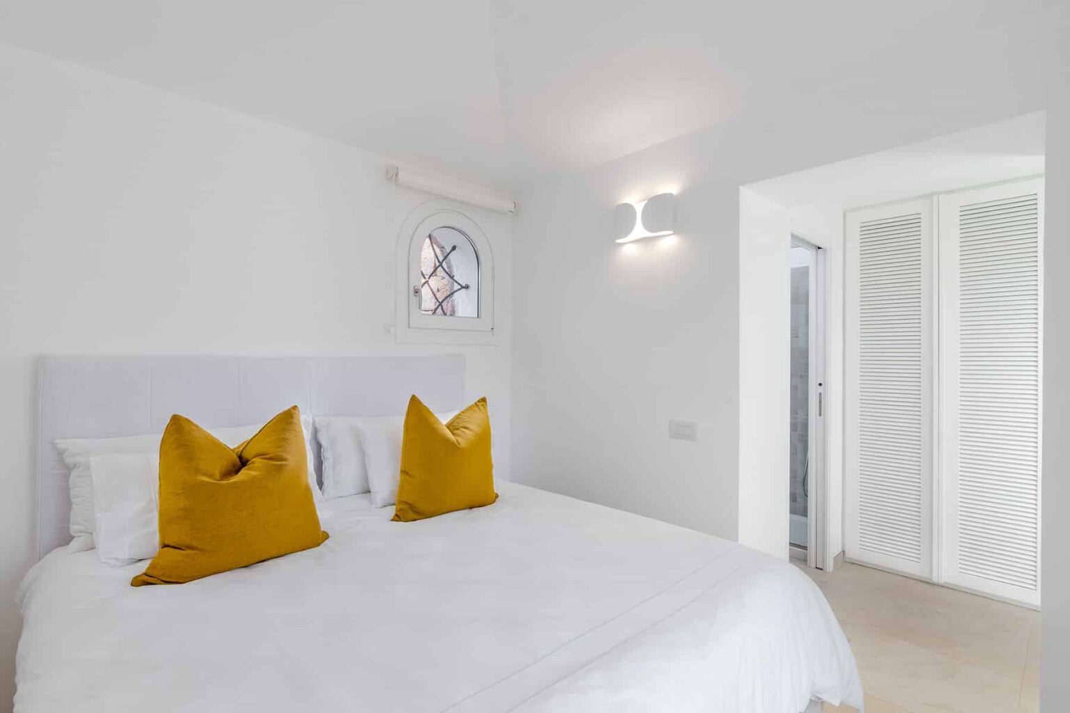 Bright and modern bedroom featuring a white bed with yellow decorative pillows, minimalist decor, and soft lighting, creating a cozy atmosphere. | Only on SopranoVillas