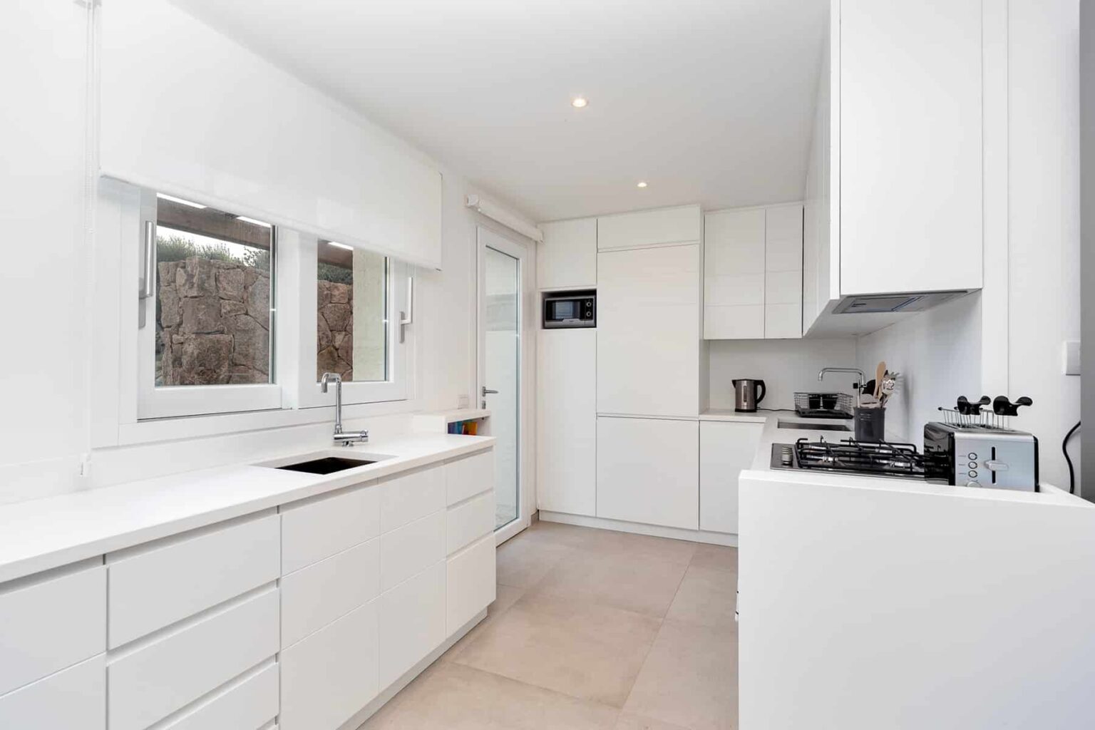 Modern white kitchen with sleek cabinetry, stainless steel appliances, and ample natural light from large windows. | Only on SopranoVillas