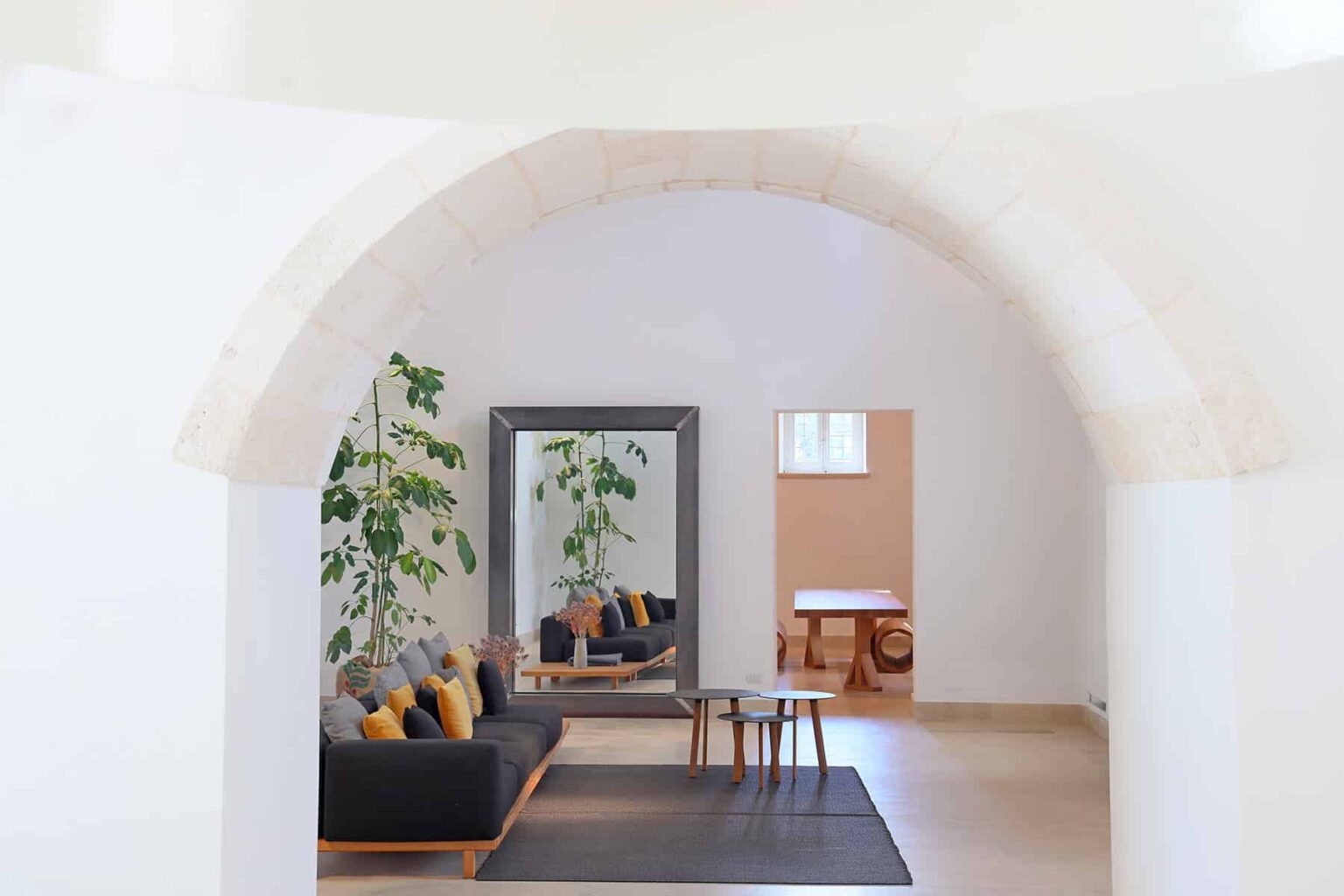 Modern living room interior featuring an arched entrance, a black sofa with colorful cushions, a large mirror, and indoor plants, creating a bright and inviting atmosphere. | Only on SopranoVillas