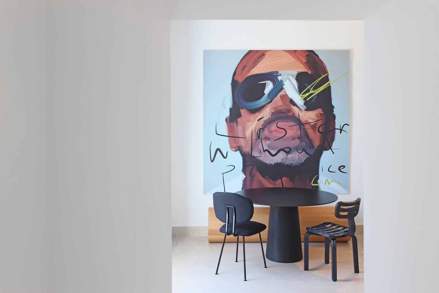 Interior view featuring a modern dining area with a round black table and stylish chairs, complemented by a large, vibrant mural of a man wearing sunglasses. The artwork adds a contemporary artistic touch to the space. | Only on SopranoVillas