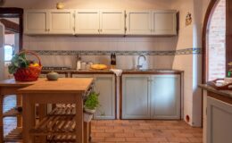 Cozy kitchen interior featuring light green cabinets, a wooden island, and tiled backsplash, with fresh produce in a basket and a bright, inviting atmosphere.