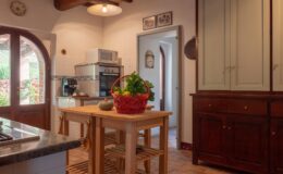 Cozy kitchen interior featuring a wooden dining table with a basket of fresh vegetables, modern appliances, and traditional cabinetry, illuminated by natural light from a window.