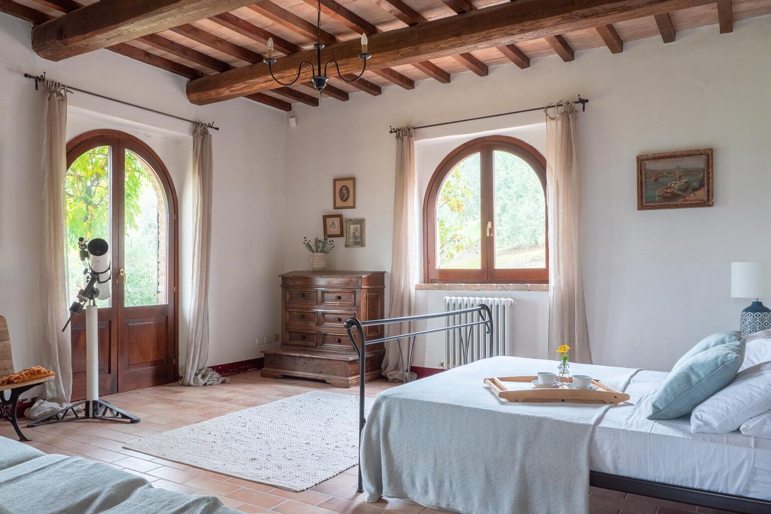Spacious and inviting bedroom featuring two beds, wooden beams, large arched windows, and tasteful decor, ideal for a relaxing getaway. | Only on SopranoVillas