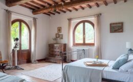 Spacious and inviting bedroom featuring two beds, wooden beams, large arched windows, and tasteful decor, ideal for a relaxing getaway.