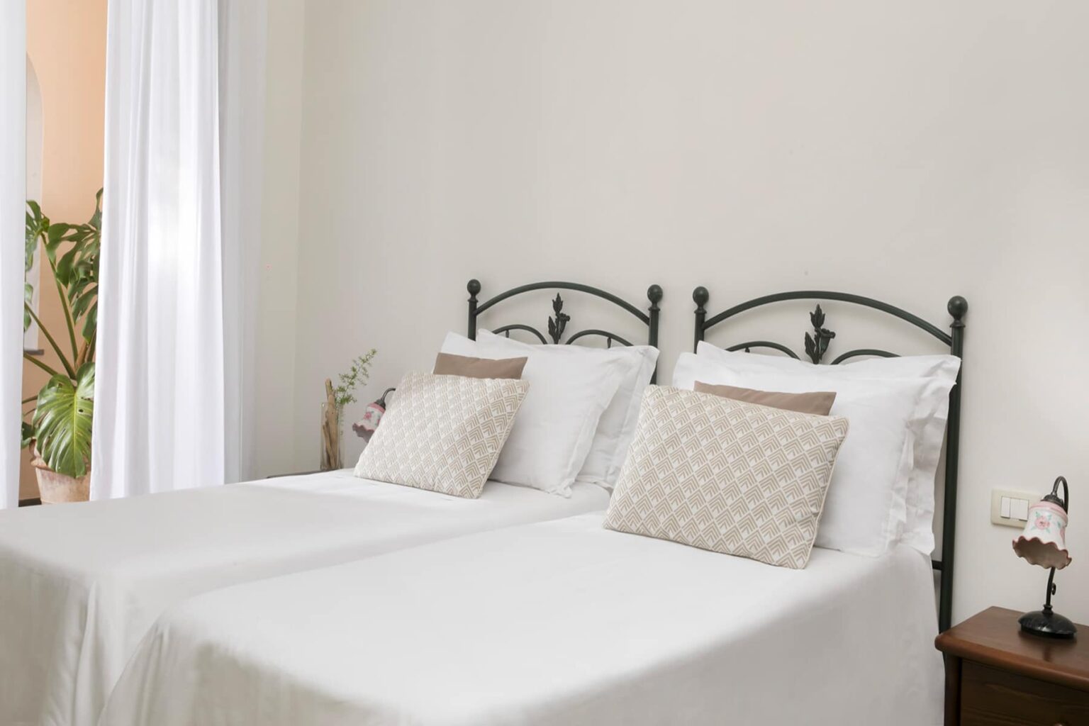 Cozy bedroom featuring two twin beds with decorative pillows, a neutral color scheme, and natural light from a nearby window, creating a warm and inviting atmosphere. | Only on SopranoVillas