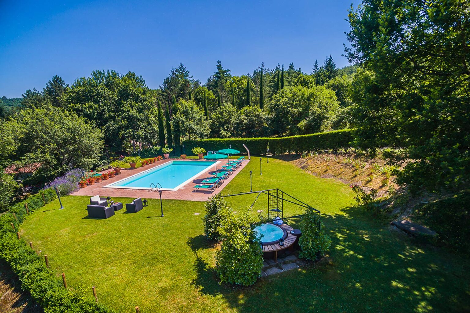 Aerial view of a serene outdoor swimming pool surrounded by lush greenery, featuring lounge chairs and a hot tub, perfect for relaxation and leisure. | Only on SopranoVillas