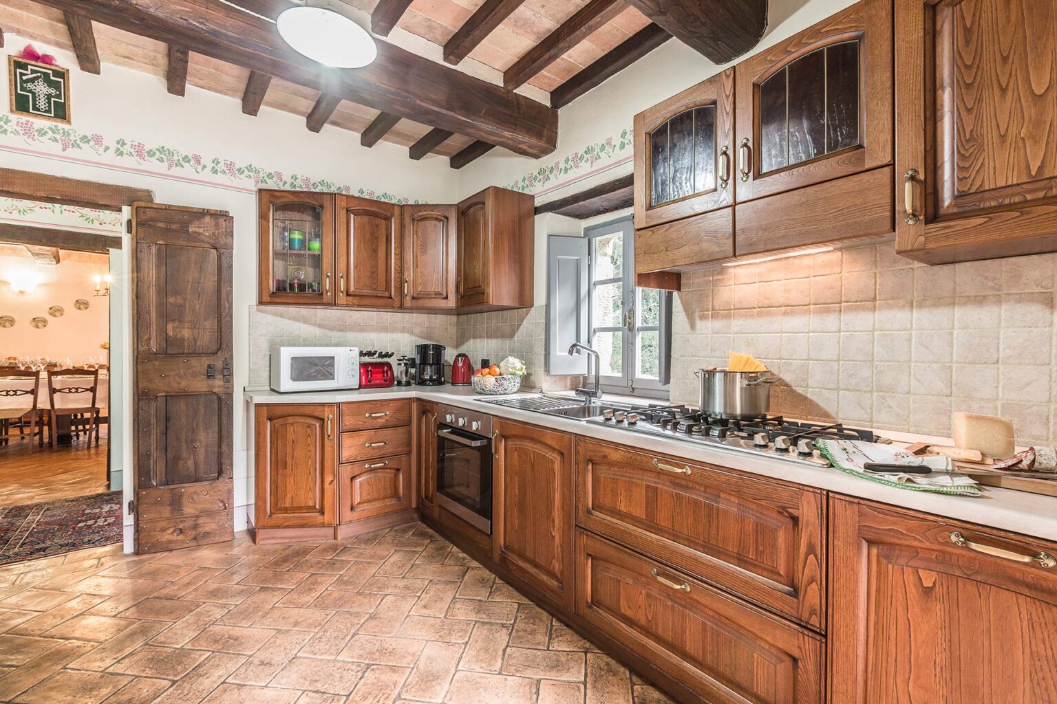Cozy kitchen interior featuring wooden cabinets, a gas stove, and a microwave, with rustic tile flooring and exposed wooden beams, creating a warm and inviting atmosphere. | Only on SopranoVillas