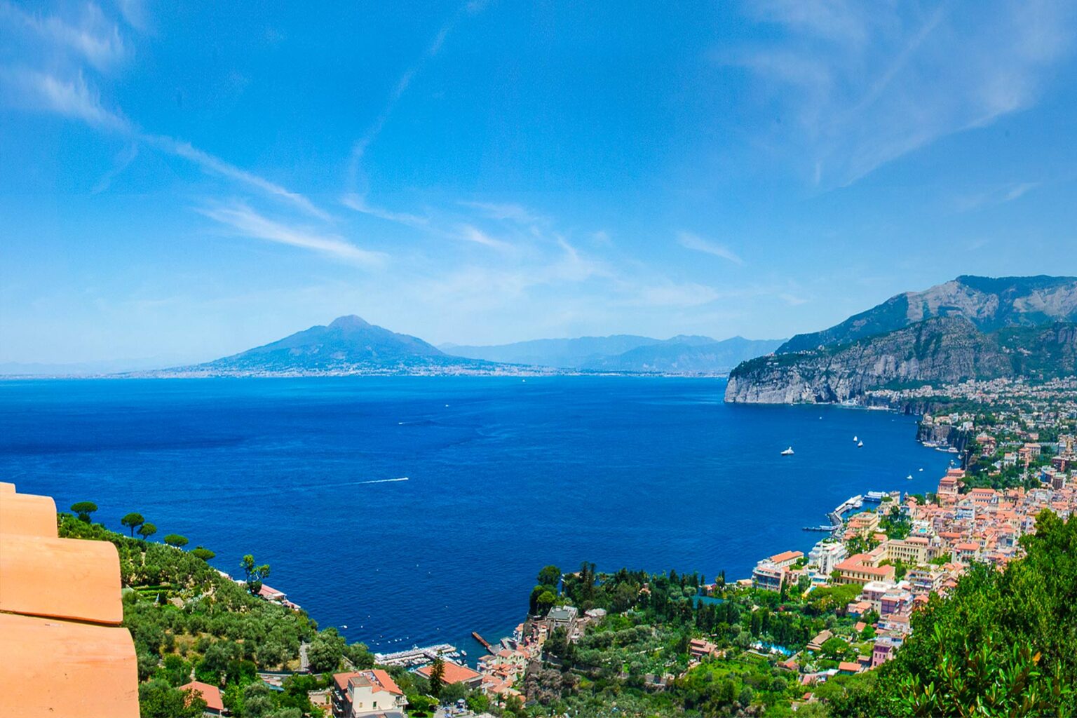 Scenic view of the coastline with vibrant blue waters, mountains in the background, and a picturesque town nestled along the shore, highlighting the beauty of the Mediterranean landscape. | Only on SopranoVillas