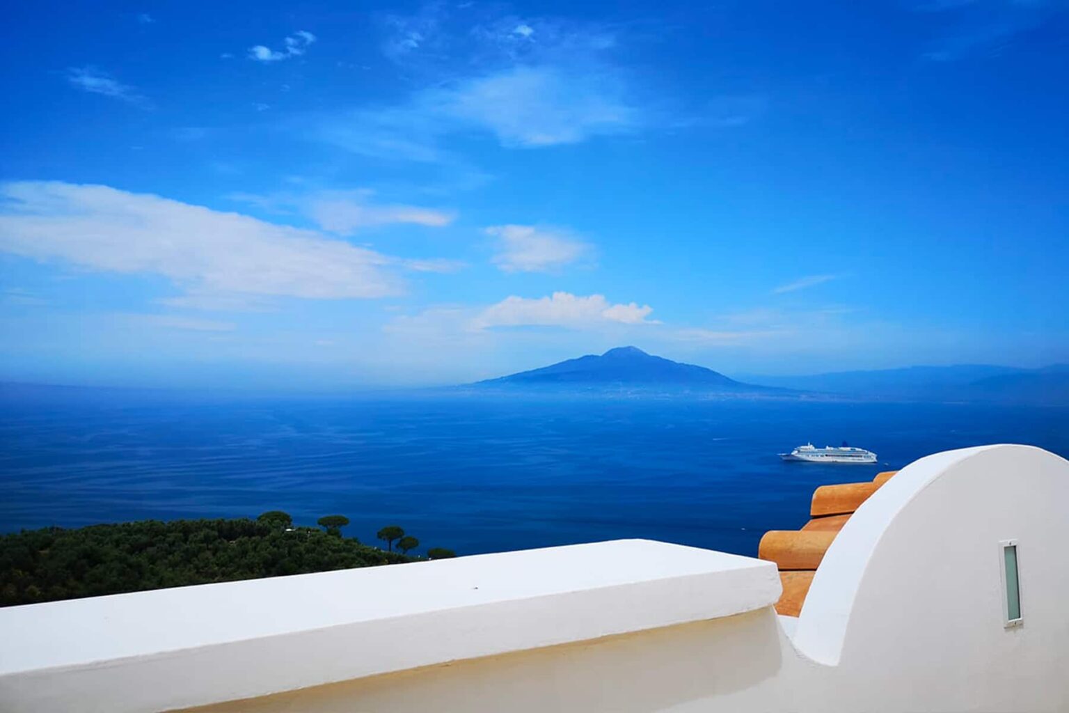 Scenic view of Mount Vesuvius rising above the blue waters of the Gulf of Naples, with a clear sky and a distant boat in the foreground. | Only on SopranoVillas