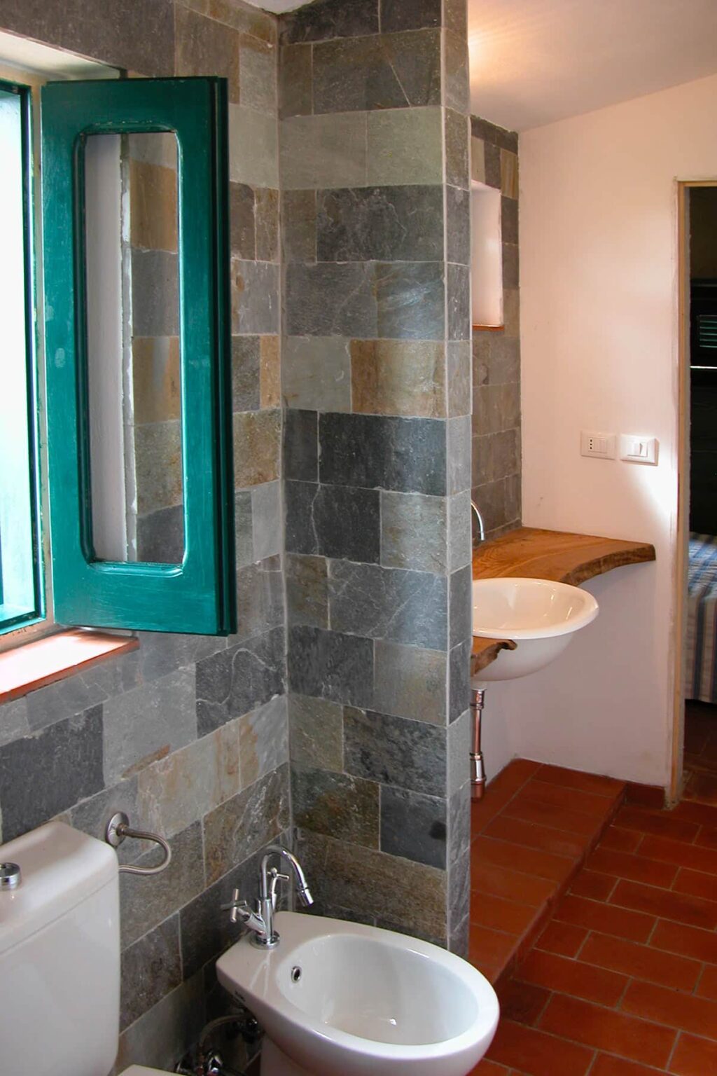 Modern bathroom featuring a slate-tiled wall, a stylish wooden countertop with a white sink, and a large green-framed window allowing natural light to brighten the space. | Only on SopranoVillas