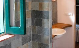 Modern bathroom featuring a slate-tiled wall, a stylish wooden countertop with a white sink, and a large green-framed window allowing natural light to brighten the space.